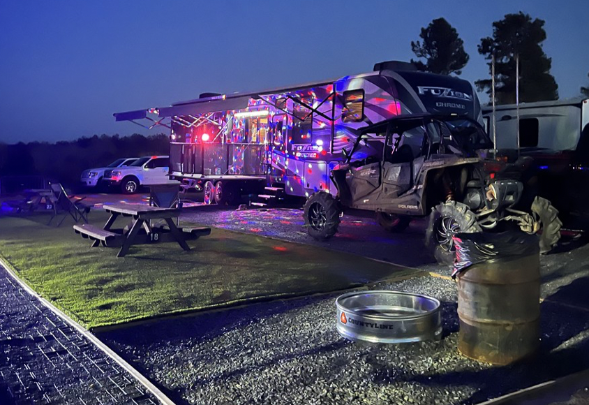 Campground site at dusk with lights on an RV and an ATV parked at the site