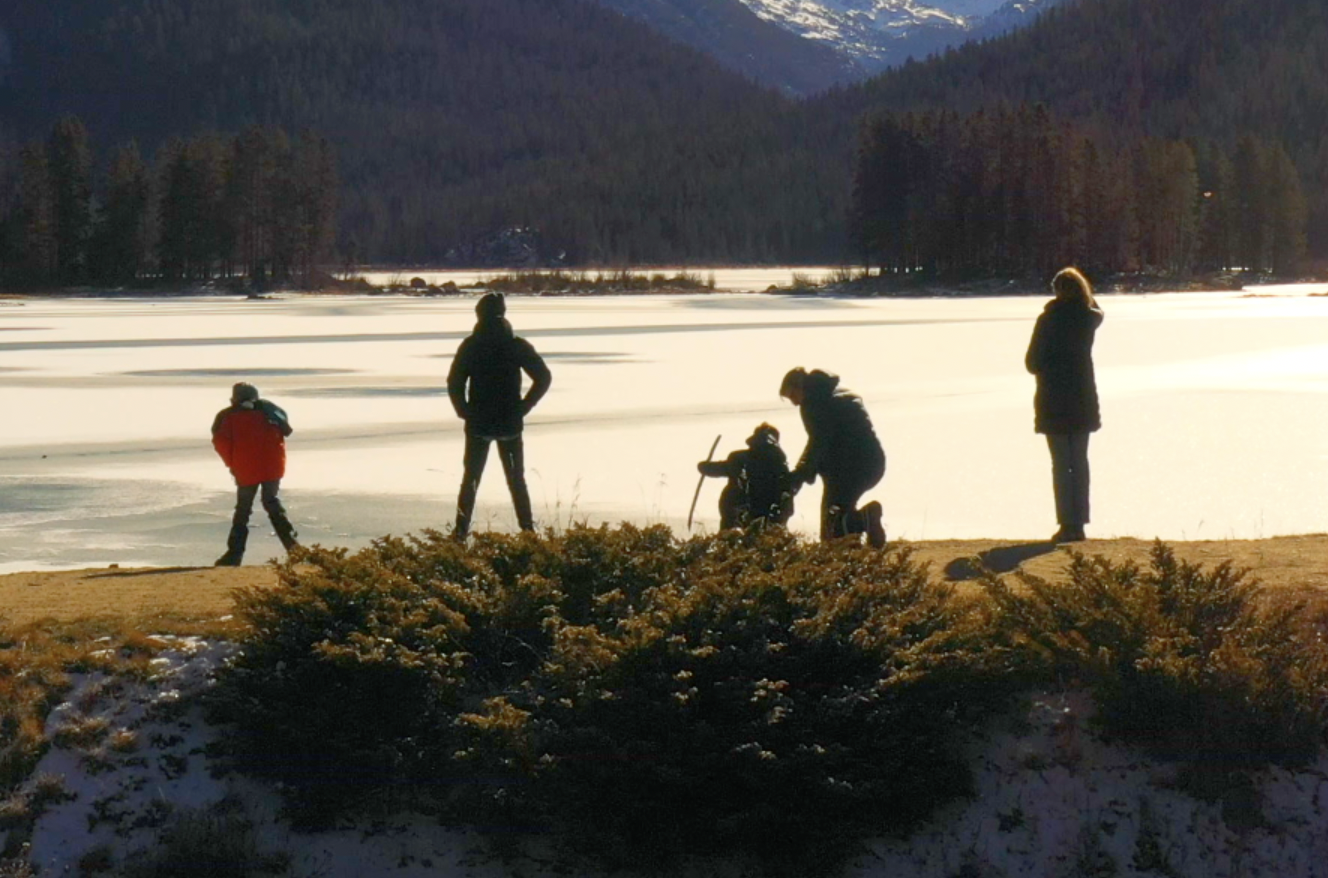 Family standing at the edge of a lake in cold weather.