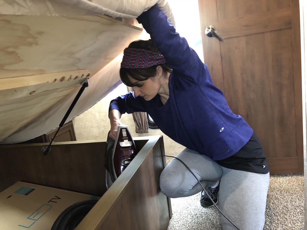 Individual vacuuming under-bed storage in an RV to remove dirt and maintain a clean living space.