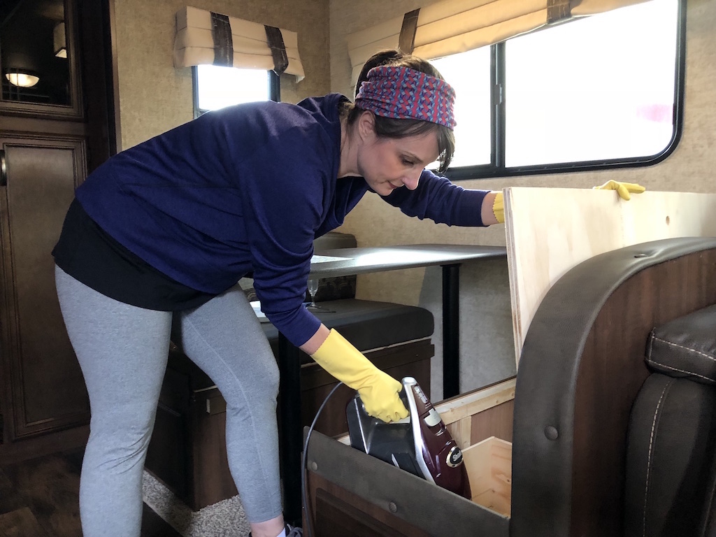 Individual organizing and cleaning the storage compartments beneath an RV dinette for efficient use of space.