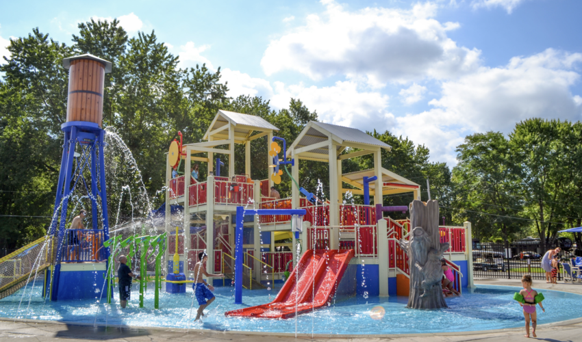 Children playing on a large water playground with multiple stories, a tower, and spray features.